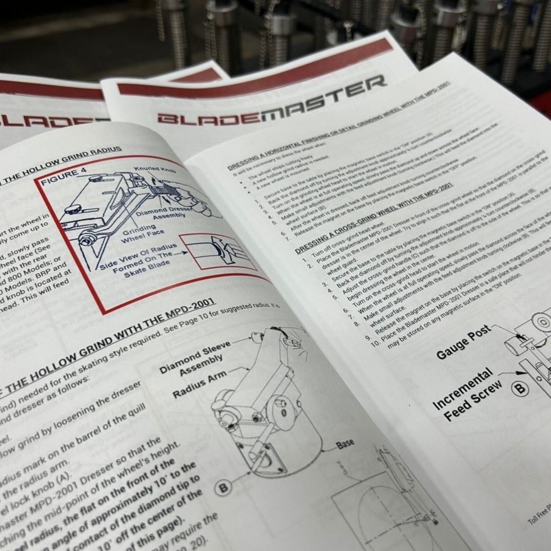 Open instruction booklet pages for Bladmaster showing assembly and grinding instructions with diagrams and text, photographed close up with blurred metal components in the background.